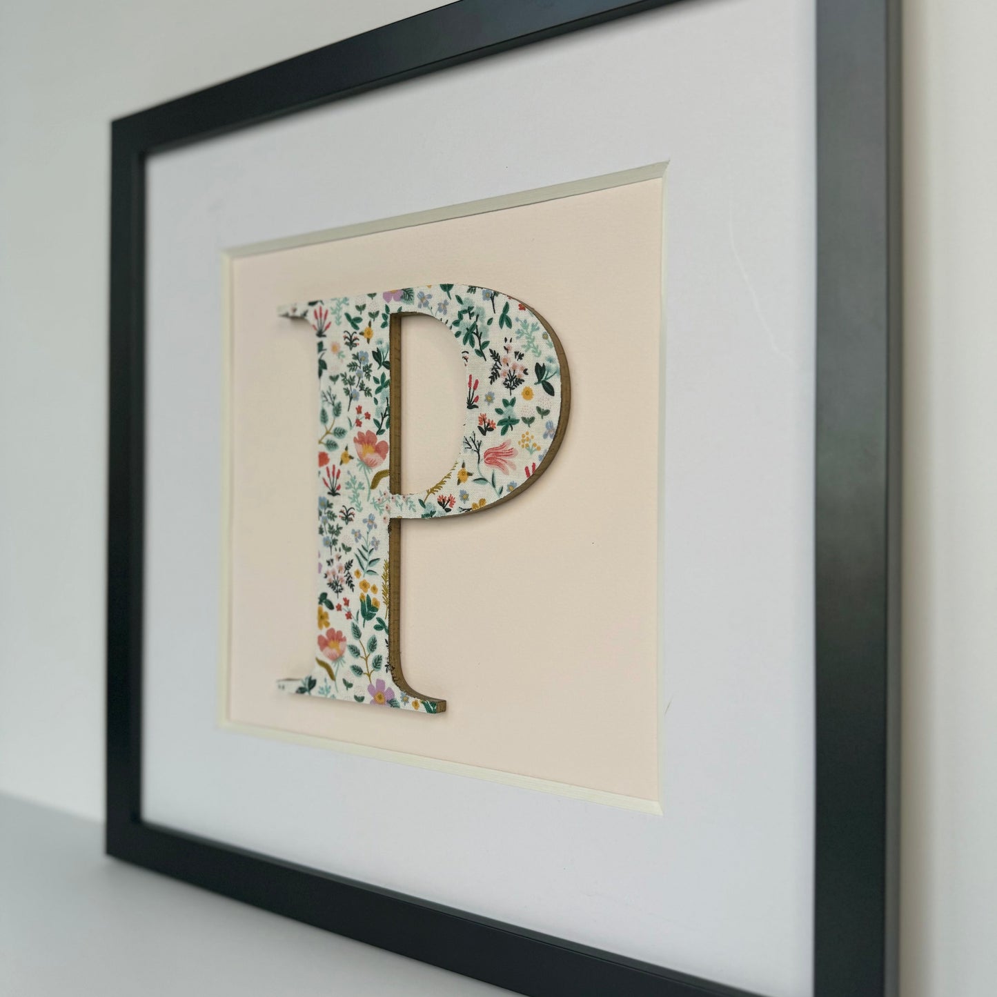 a black framed floral letter p on pale pink background