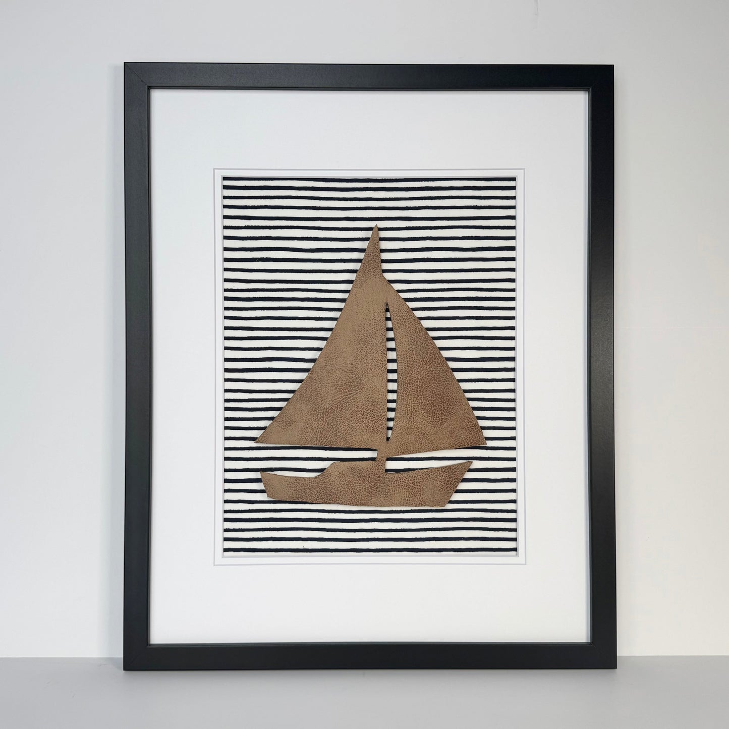 Black framed leather sailboat on a navy blue striped fabric background