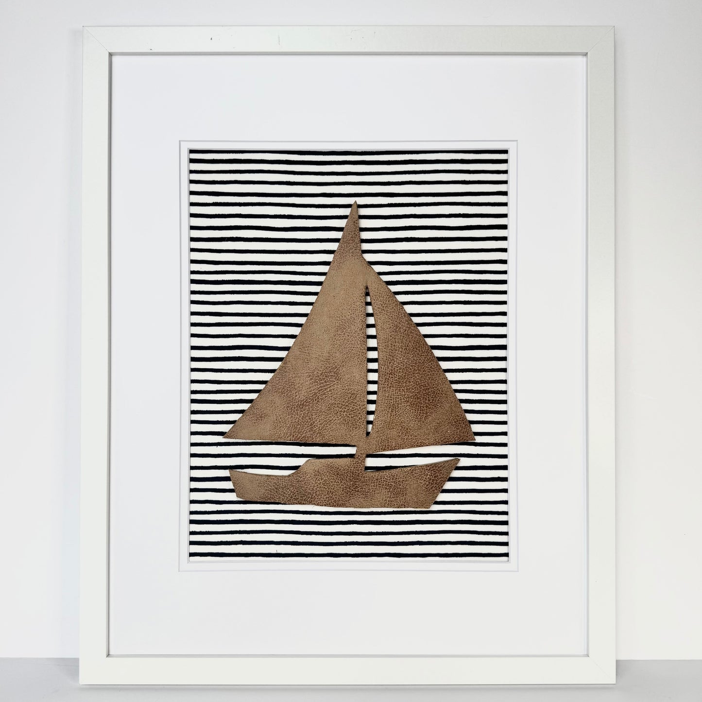 White framed leather sailboat on a navy blue striped fabric background