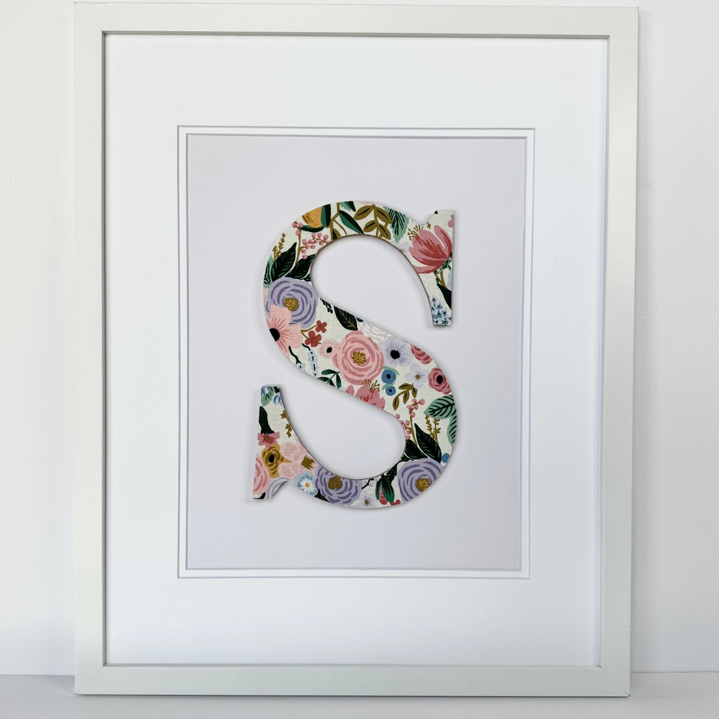 White Framed letter S with a pink and lavender floral pattern on a pale lavender background