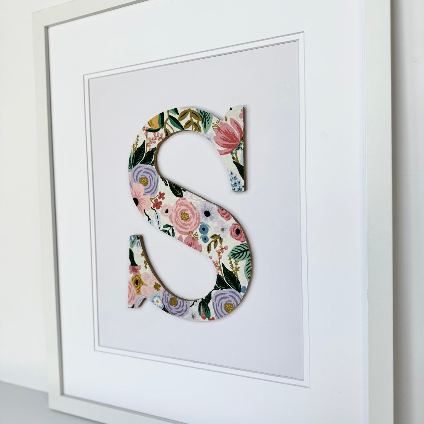 White Framed Nursery letter S with a pink and lavender floral pattern on a pale lavender background