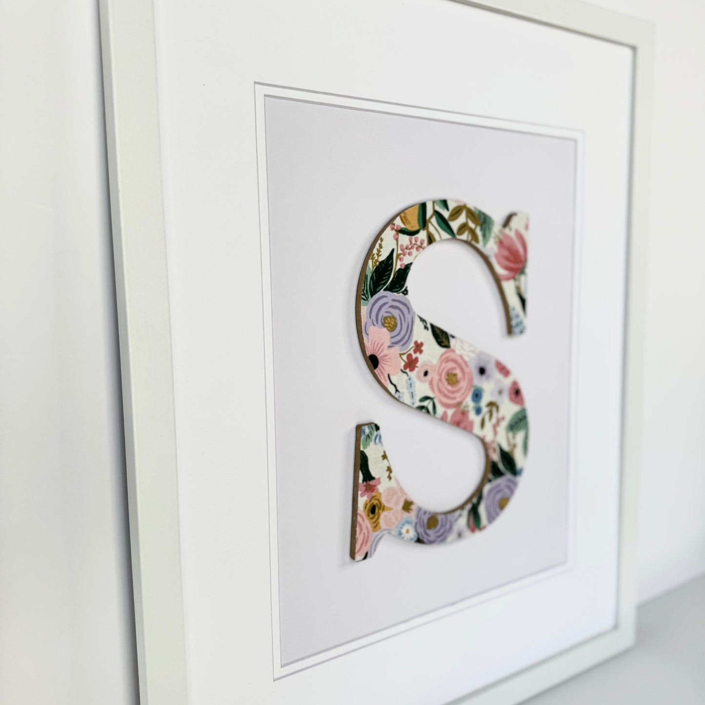White Framed Nursery letter S with a pink and lavender floral pattern on a pale lavender background
