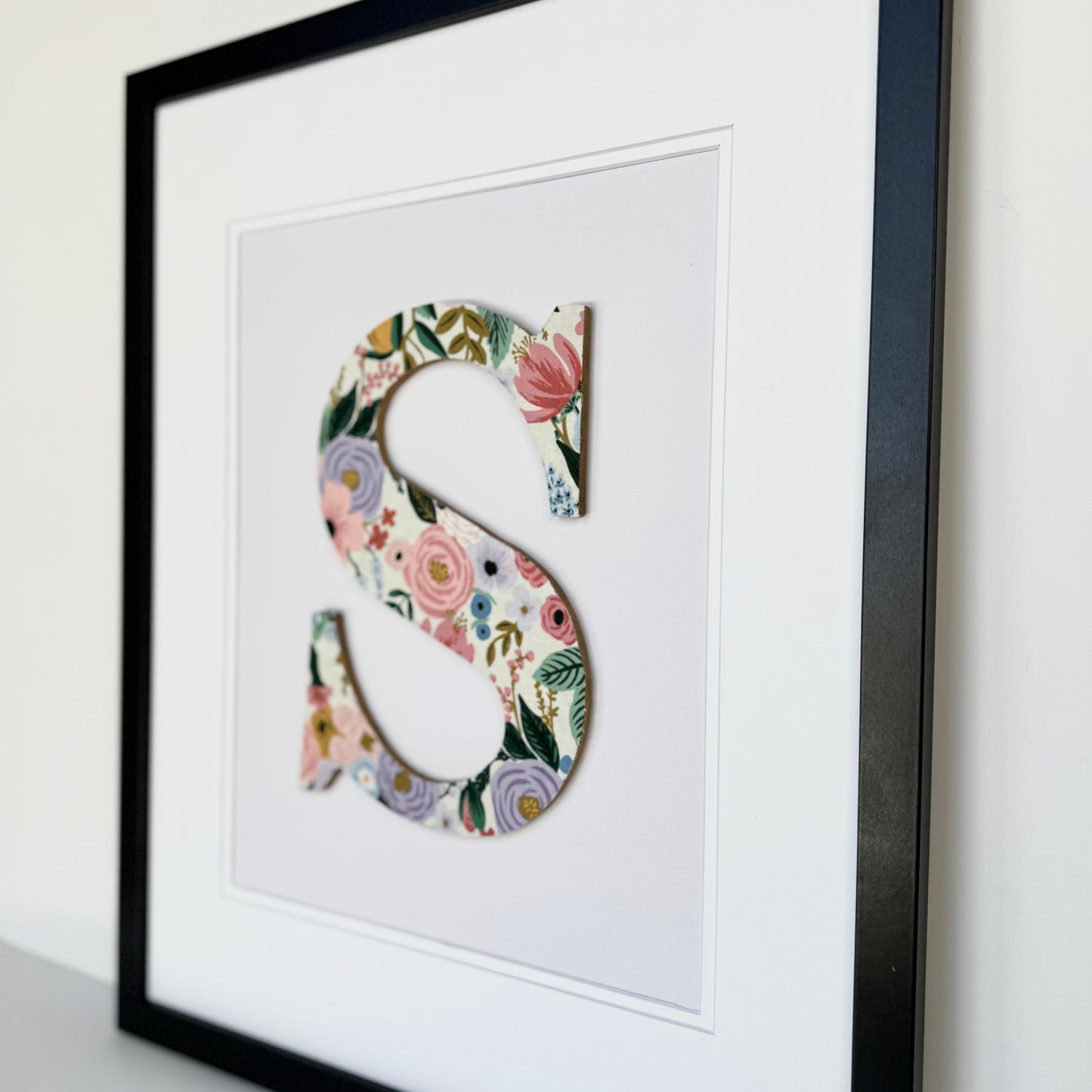 Black Framed letter S with a pink and lavender floral pattern on a pale lavender background