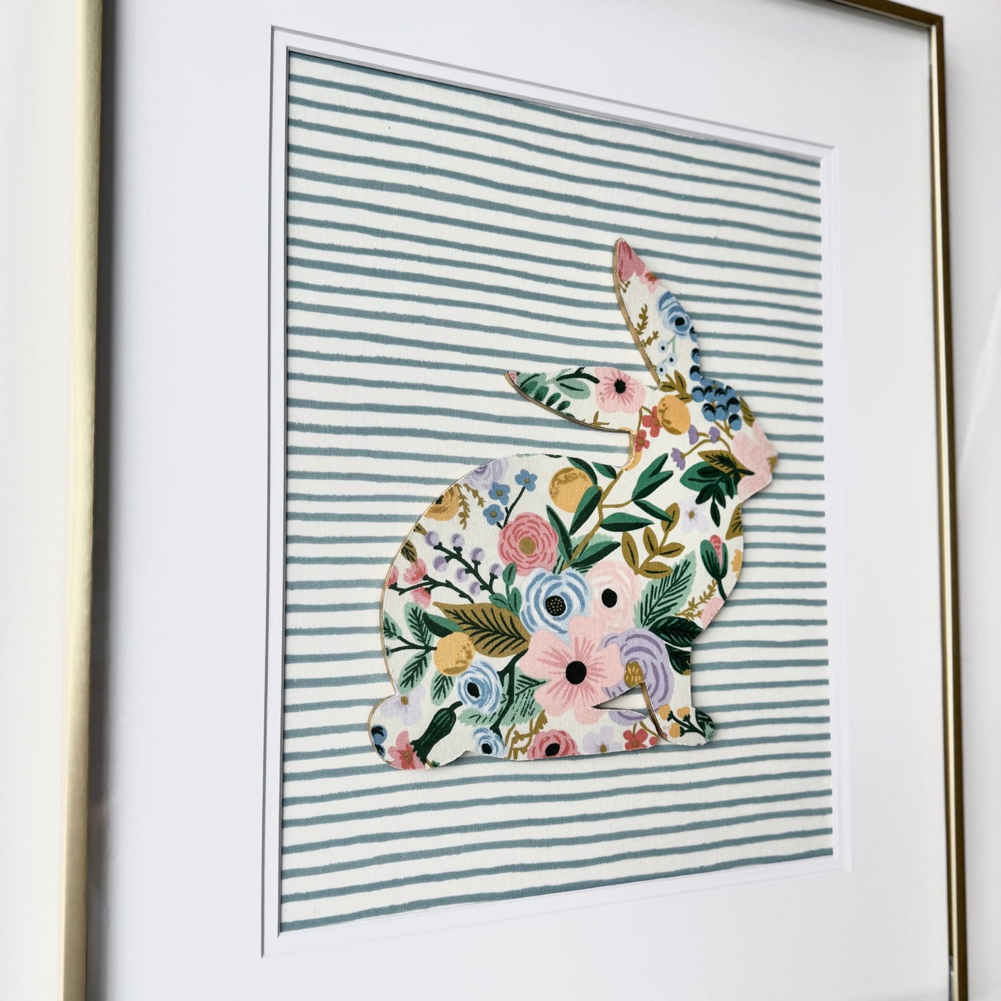 Gold framed Rifle Paper Co. Floral bunny on a blue striped background, hanging on a wall