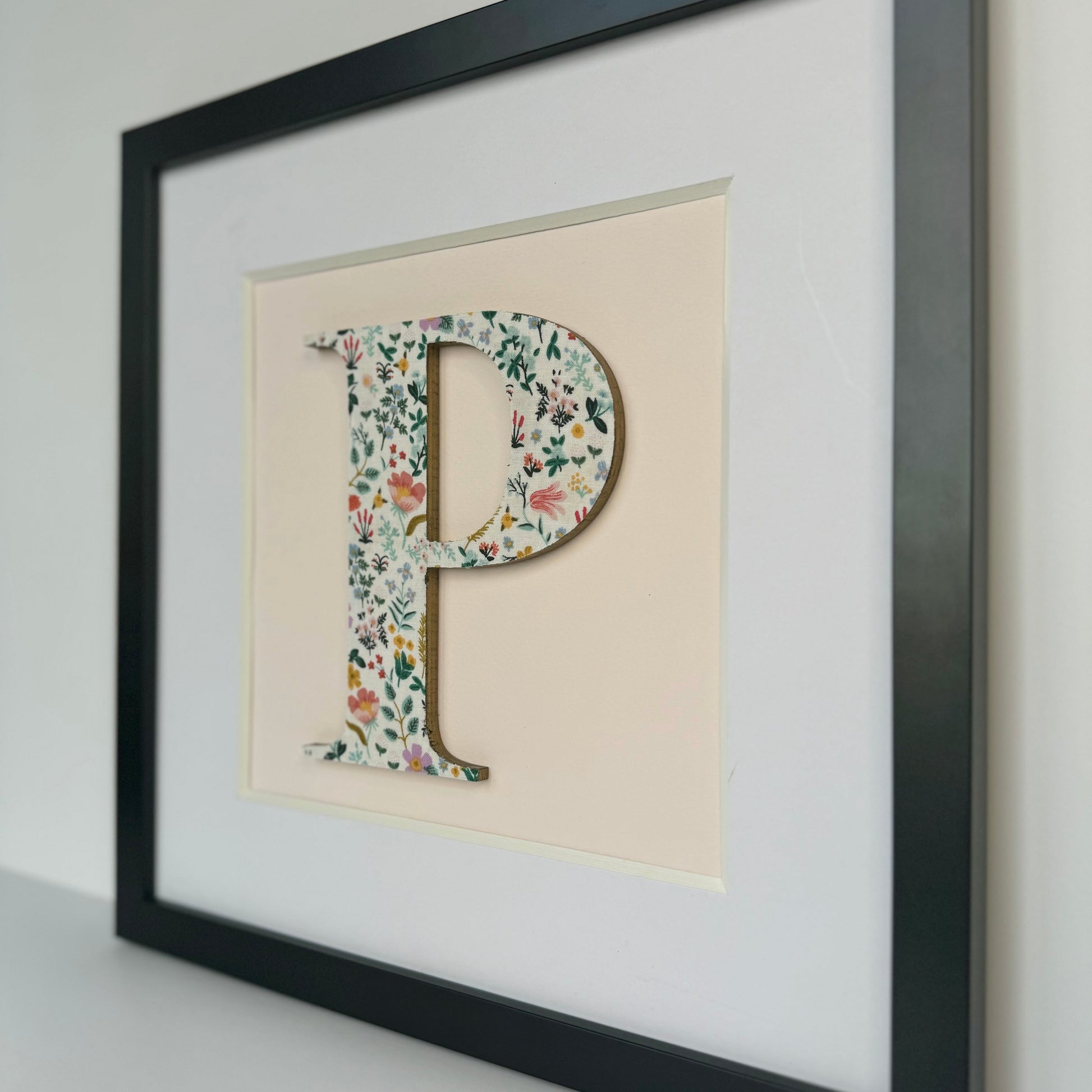 a black framed floral letter p on pale pink background