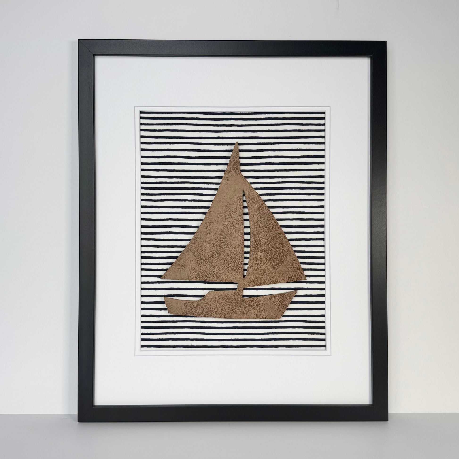 Black framed leather sailboat on a navy blue striped fabric background