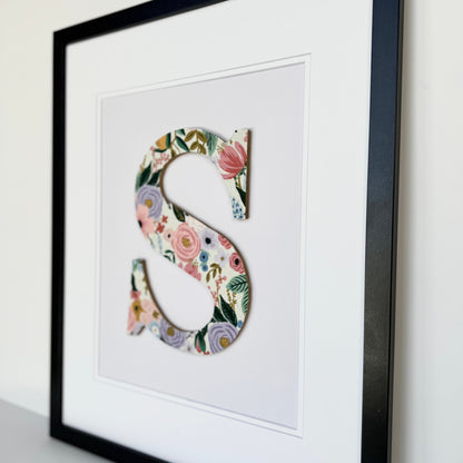 Black Framed letter S with a pink and lavender floral pattern on a pale lavender background