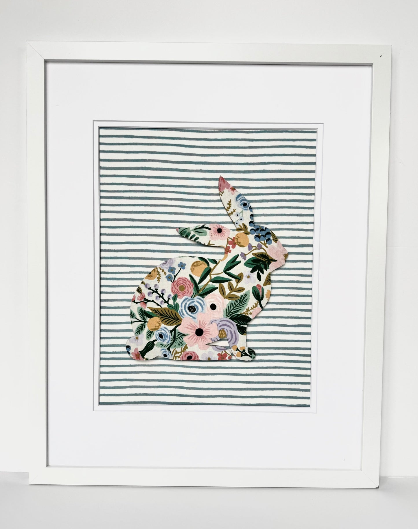 White, framed Rifle Paper Co. Floral bunny on a blue striped background, hanging on a wall