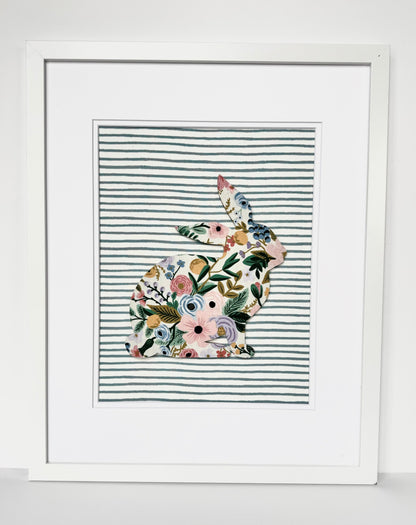 White, framed Rifle Paper Co. Floral bunny on a blue striped background, hanging on a wall