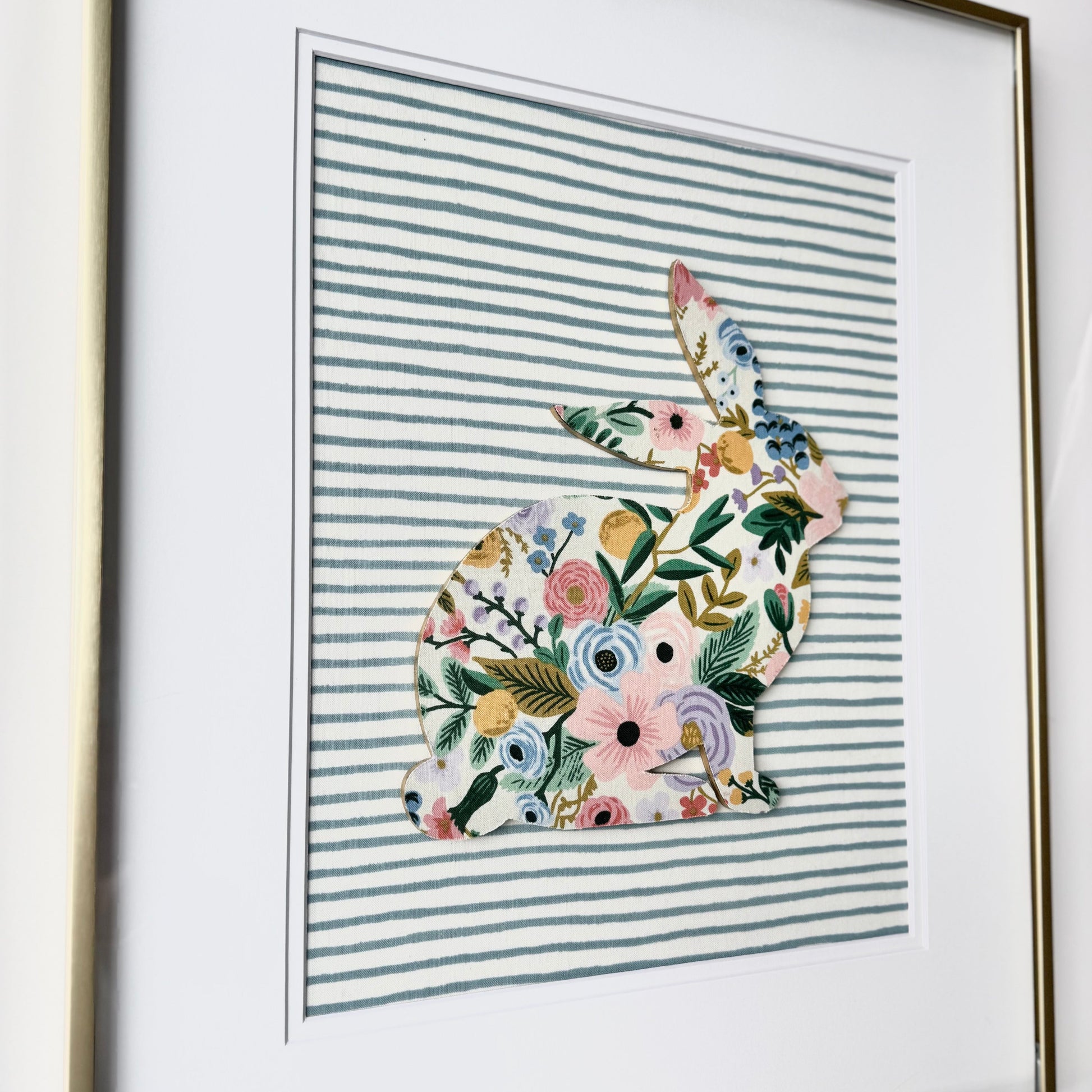 Gold framed Rifle Paper Co. Floral bunny on a blue striped background, hanging on a wall