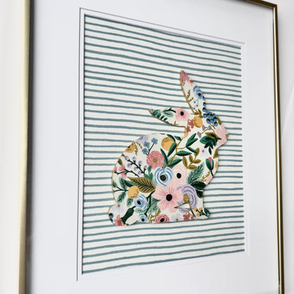 Gold framed Rifle Paper Co. Floral bunny on a blue striped background, hanging on a wall